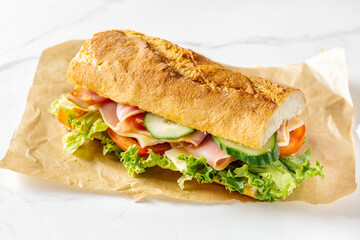Big sandwich with lettuce, tomatoes prosciutto cucumber and cheese on light background