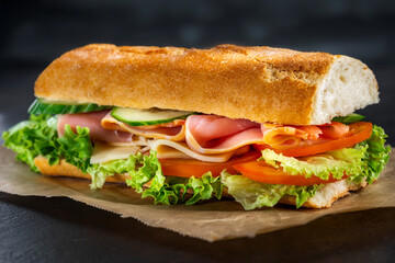 Big sandwich with lettuce, tomatoes prosciutto cucumber and cheese on a dark background