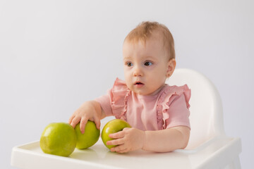 Fototapeta na wymiar Cute baby in a baby chair nibbles apples on a white background