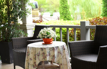 A vintage style balcony decorated with dark rattan chairs and a floral table cover. and a coffee...