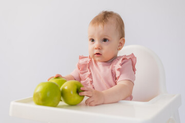 Cute baby in a baby chair nibbles apples on a white background