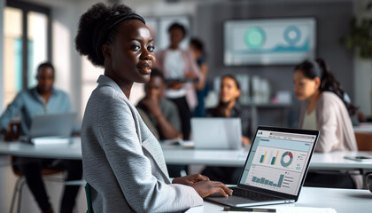 of an African businesswoman confidently presenting financial forecasts on her laptop to invisible stakeholders, with colleagues collaborating on related projects in the background,