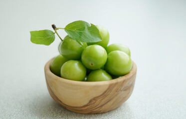 Green plums. A bowl of fresh unripe plums on a white background. Fresh raw green plum in wooden bowl. Top view.