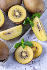 Ripe raw kiwi gold whole and slices on vintage silver metalic tray with mint leaves on rustic stone...