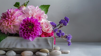 A beautiful arrangement of pink dahlias and roses accompanied by purple flowers and white stones on a neutral background, perfect for serene design themes. 