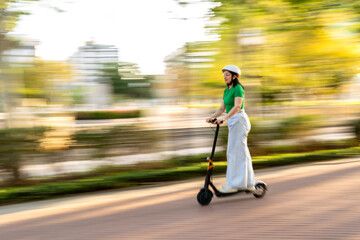 In motion. a young woman enjoys a lively scooter ride through the park, her helmet ensuring a safe journey. © pablo