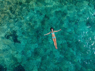 AERIAL, TOP DOWN: Young woman floating peacefully in the bright blue clear sea