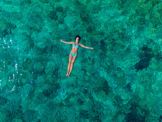 AERIAL, TOP DOWN: A bikini doting woman floats in clear turquoise Croatian sea