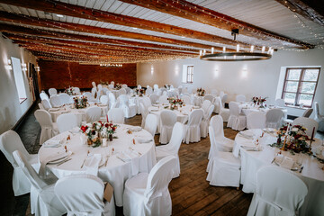 Valmiera, Latvia - August 19, 2023 - Indoor wedding venue decorated with white draped chairs, round...