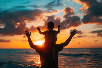 silhouette of father with son on his shoulders, both hands outstretched in the air against a sunset background at the beach. 