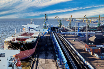 Coal harbor at maritime dry bulk terminal, bulk carrier under loading.