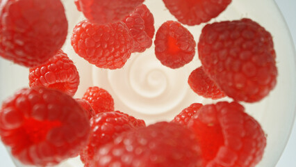 Fresh raspberries falling into yoghurt cream, top down view