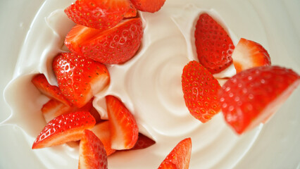 Fresh strawberries falling into yoghurt cream, top down view