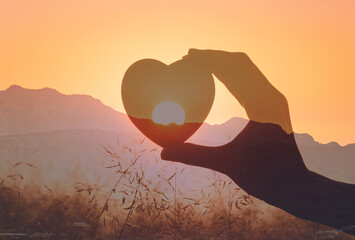 Hand holding heart up to beautiful sunrise. Love, donation, gift, charity concept.	