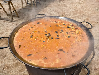 large seafood paella cooking at the moment the broth is boiling, outdoor image (typical Spain)