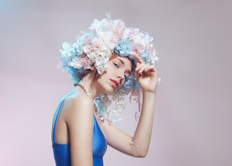 Naklejka premium A beautiful woman with a wreath of flowers in a blue swimsuit on a pink background