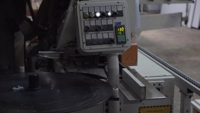Automatic edge bander on furniture production. Worker adjusts the woodworking machine in the background.