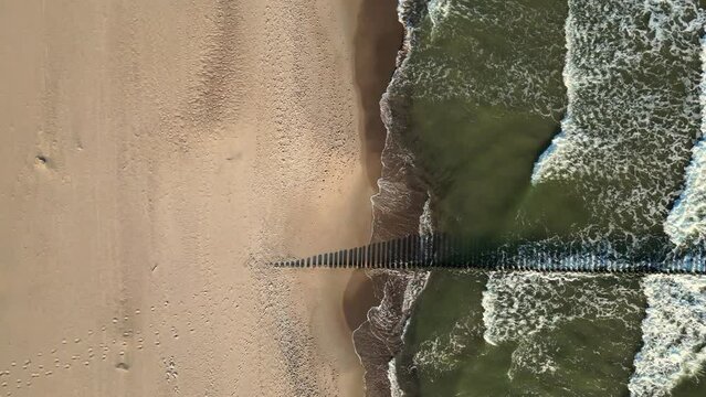 Drone footage over Rewal's Baltic Sea coastline, showcasing deserted sandy beaches, wooden breakwaters, and tranquil waves. The scene is in morning light with almost empty beach on Baltic in 4K 60 fps