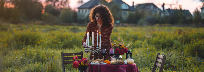 Romantic atmosphere, candles, pumpkins as decor. Sunset, golden hour banner. Beautiful young woman...