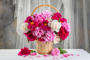 A basket of peonies flowers with pink and white flowers in it