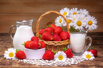 A basket of strawberries and a pitcher of milk are on a table and bouquet with daisies