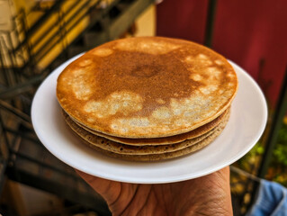 A hand holds a plate of pancakes/