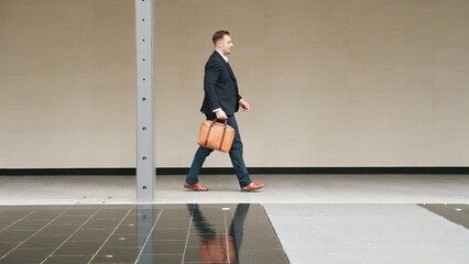 Side view of business people holding suitcase and walking to workplace along the street in urban...
