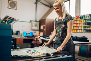 Print shop worker putting screen printed t-shirt into drying machine.