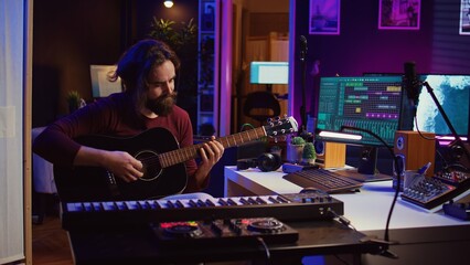 Music producer tuning his acoustic guitar before playing instrument, recording and mixing tunes to...