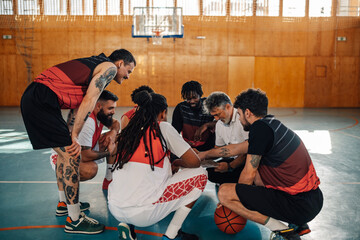 Mature basketball coach and his diverse team having a team talk during practice