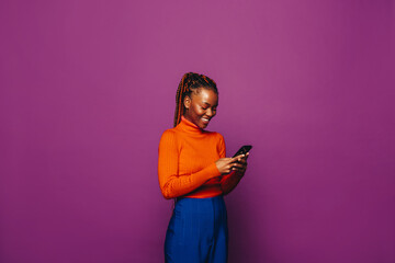 Cheerful young woman messaging on a smartphone against a vibrant purple background
