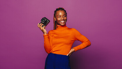 Cheerful woman with braided hair smiling and taking a picture on a vibrant purple background
