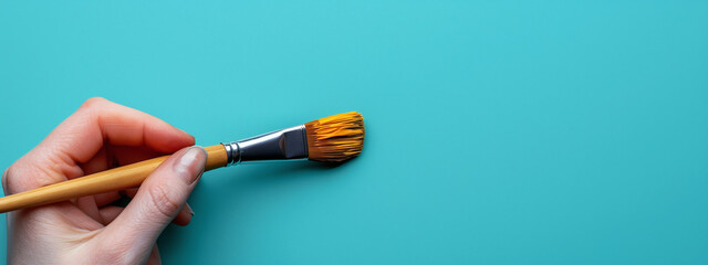 Hand Holding Yellow Paintbrush on Teal Background Art Concept