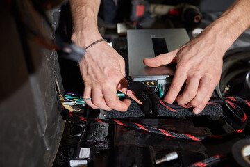 Auto electrician is connecting a wiring to car amplifier close up.