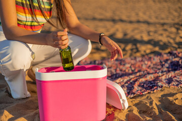 Anonymous Woman Retrieving Cold Beer from Portable Cooler on Beach at Summer Sunset
