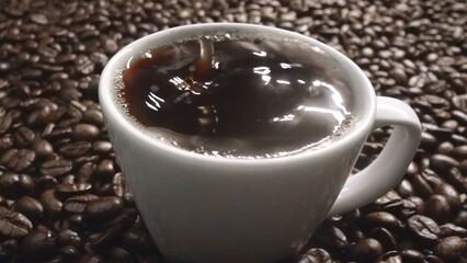 Close up of coffee bean drop in to hot espresso with pile of coffee seed. Macro of freshly roasted...