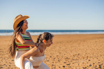 copyspace multicultural Latina lesbian couple shares laughter and joy as they ride piggyback on the beach on sunny summer day. Their bond transcends cultural boundaries, radiating warmth and happiness