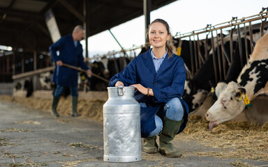 Joyful caucasian woman squatting at milk can in dairy farm in cowshed.