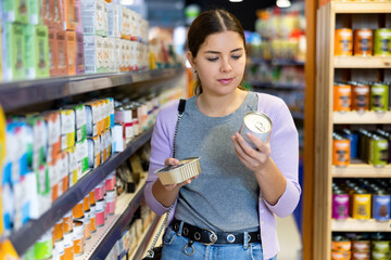 Caring young woman visiting pet store in search of tasty and healthy canned wet food for her dog