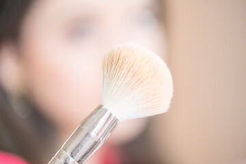 A blurred young teenager shows a soft makeup brush up close to the camera