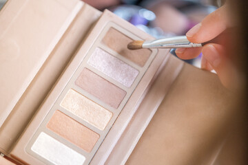 Detail of a woman's hand picking up some makeup from a makeup palette with earthy brown and golden...