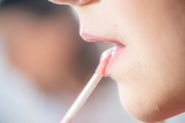 Detail of a young teenager in profile painting her lips with a small brush of light pink gloss