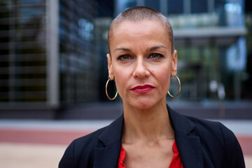 Portrait of empowered Caucasian adult business woman with modern shaved hair in formal suit looking...