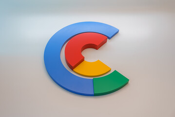 Three dimensional Google logo with colorful G displayed on a wall. Soft shadow and ambient lighting accents the design. Neutral gradient background.