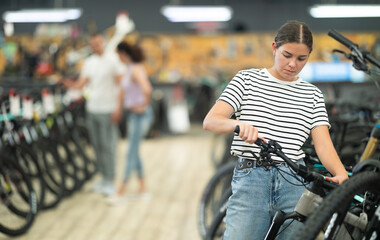 Attentive young girl examining selected bike in modern store sports goods