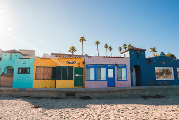 Colorful beachfront houses in turquoise, yellow, purple, and blue hues under a clear sky. Rustic...