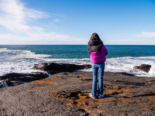 Teenager girl enjoy stunning nature of Kilkee coast and cliff, county Clare, Ireland. Rough coastline and blue cloudy sky. Travel and tourism. Irish landscape scene. Warm day. - obrazy, fototapety, plakaty