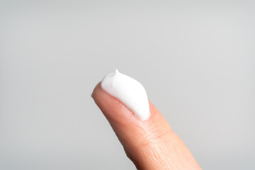 A finger showing a scoop of white moisturizing cream on a grey background