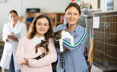 Happy preteen girl and her mother standing in shelter for abandoned animals, holding cute mottled...