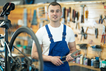 Young man bicycle repair service worker in uniform posing with tool
